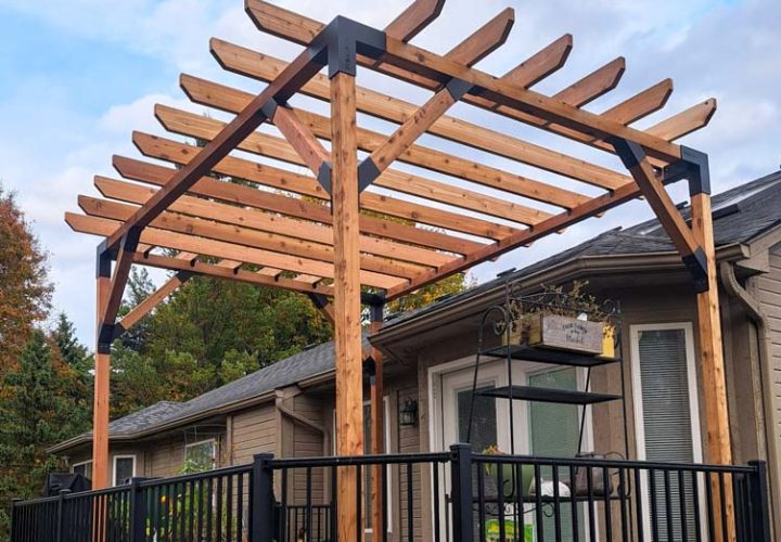 A custom-built wooden pergola with slatted roof and black metal connectors, installed over a deck with black railings. The structure provides shade and style to a backyard space, complementing the home’s exterior and enhancing outdoor comfort.